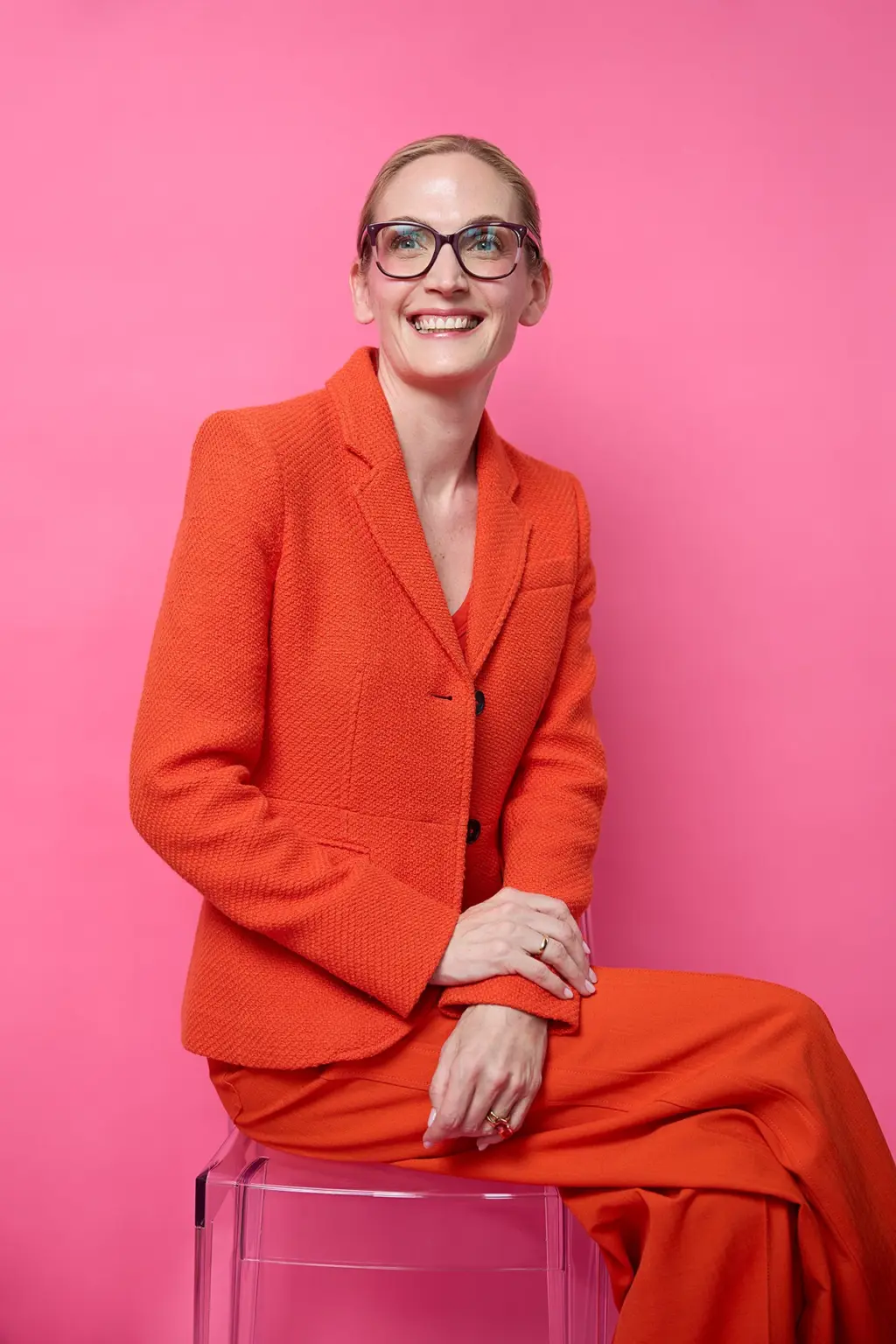 Prof. Dr. med. Anke Lührs mit Brille im orangefarbenen Blazer vor rosa Hintergrund