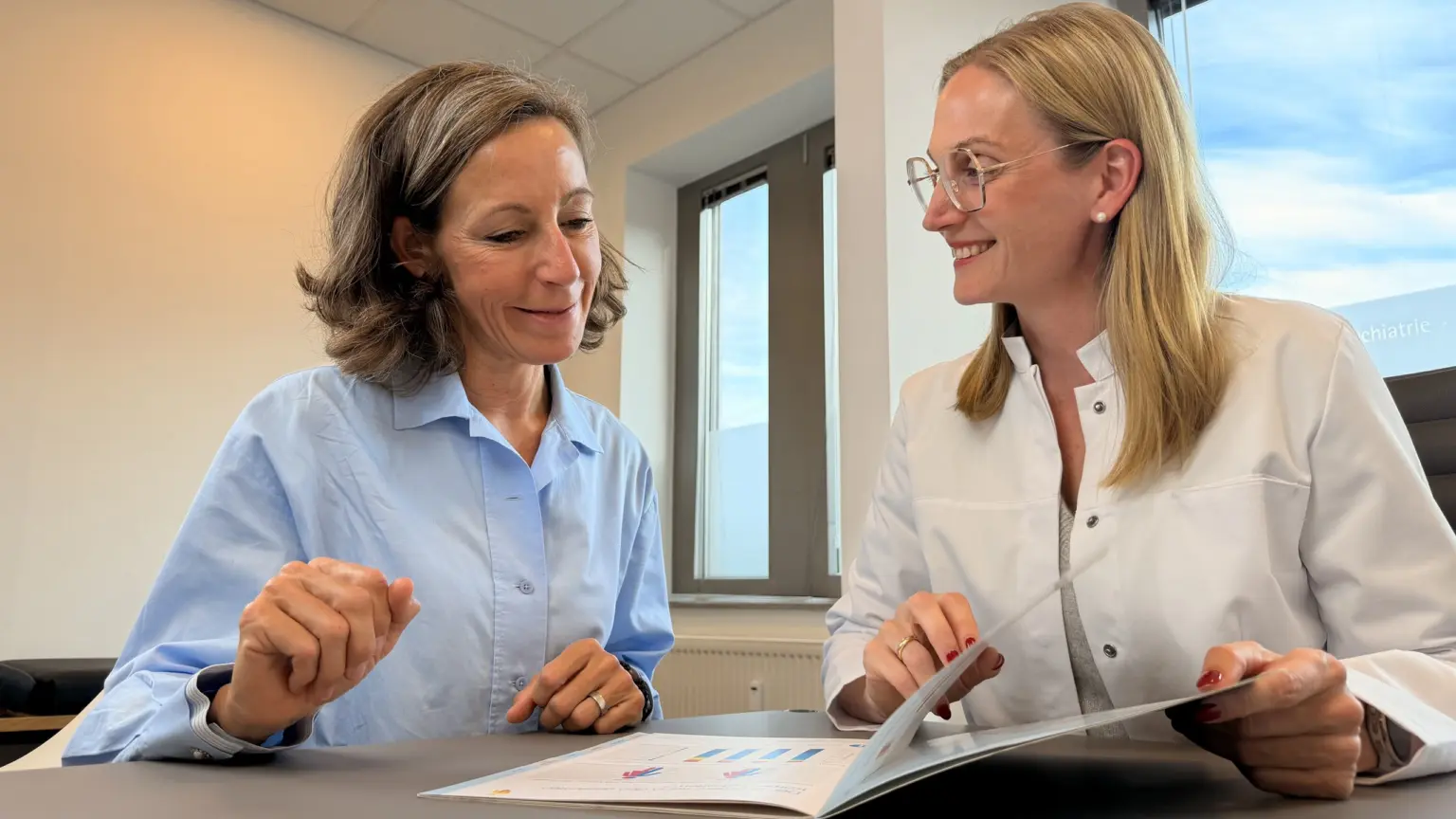 Zwei Frauen im Gespräch an einem Tisch, vor ihnen Unterlagen